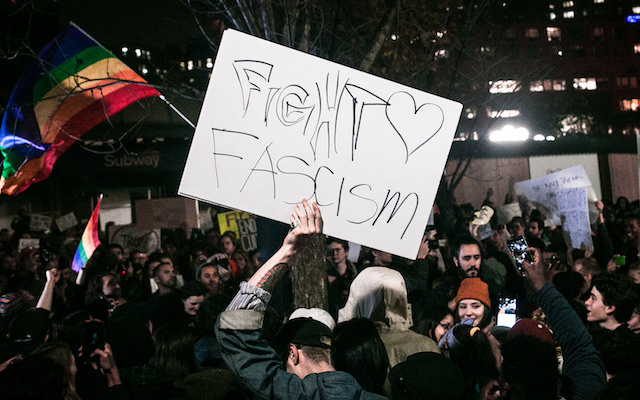 Fight Fascism on a sign held by a protester in front of a rainbow flag