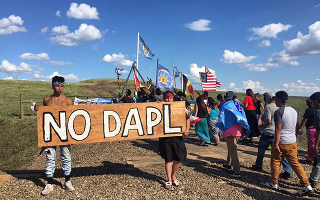 Standing Rock protestors holding a hand-painted NO DAPL sign