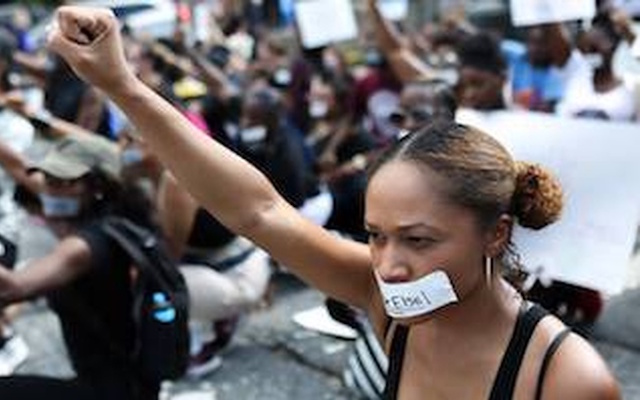 Black woman with a raised fist and tape over her mouth